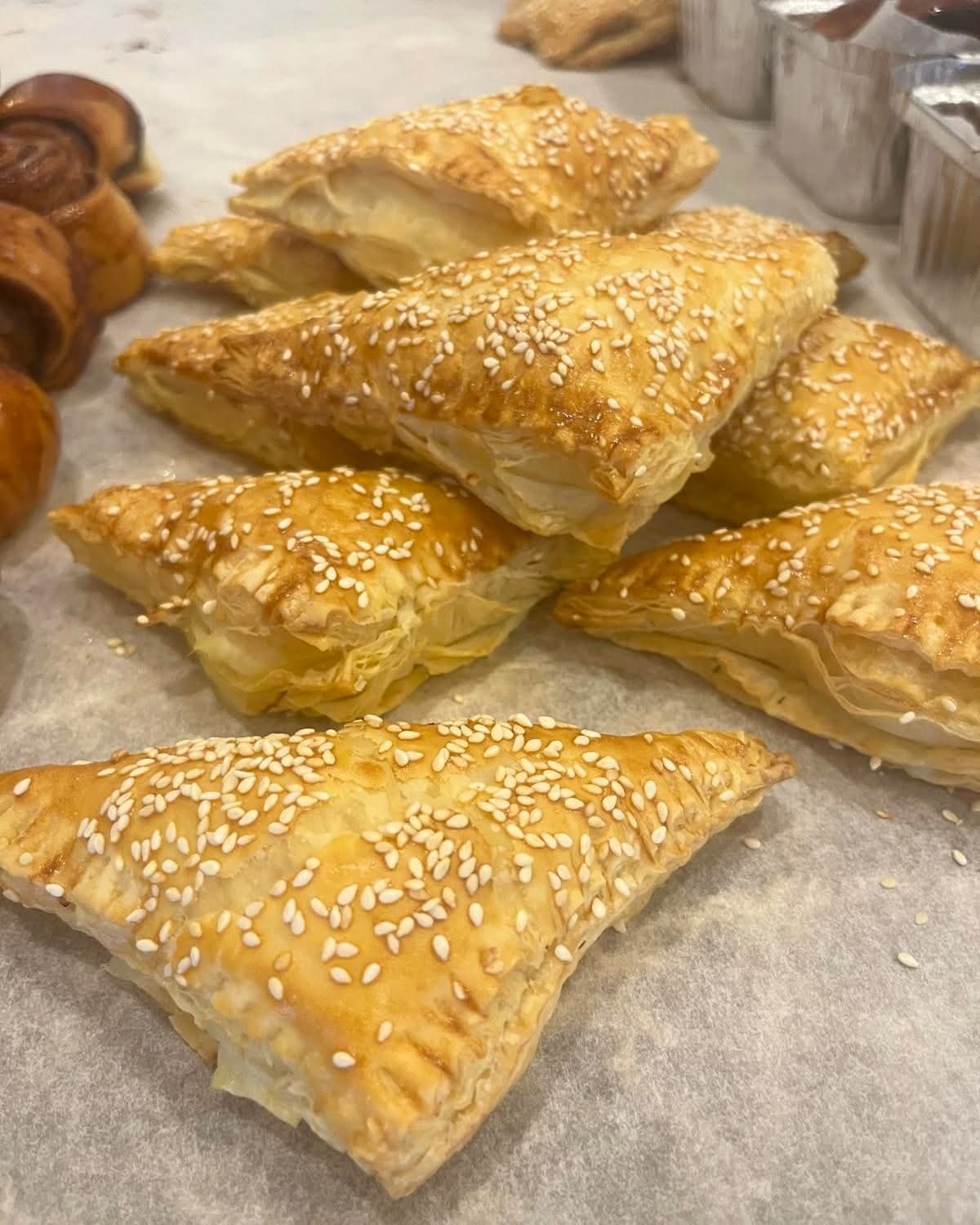 Golden, flaky triangular pastries generously topped with white sesame seeds on parchment.