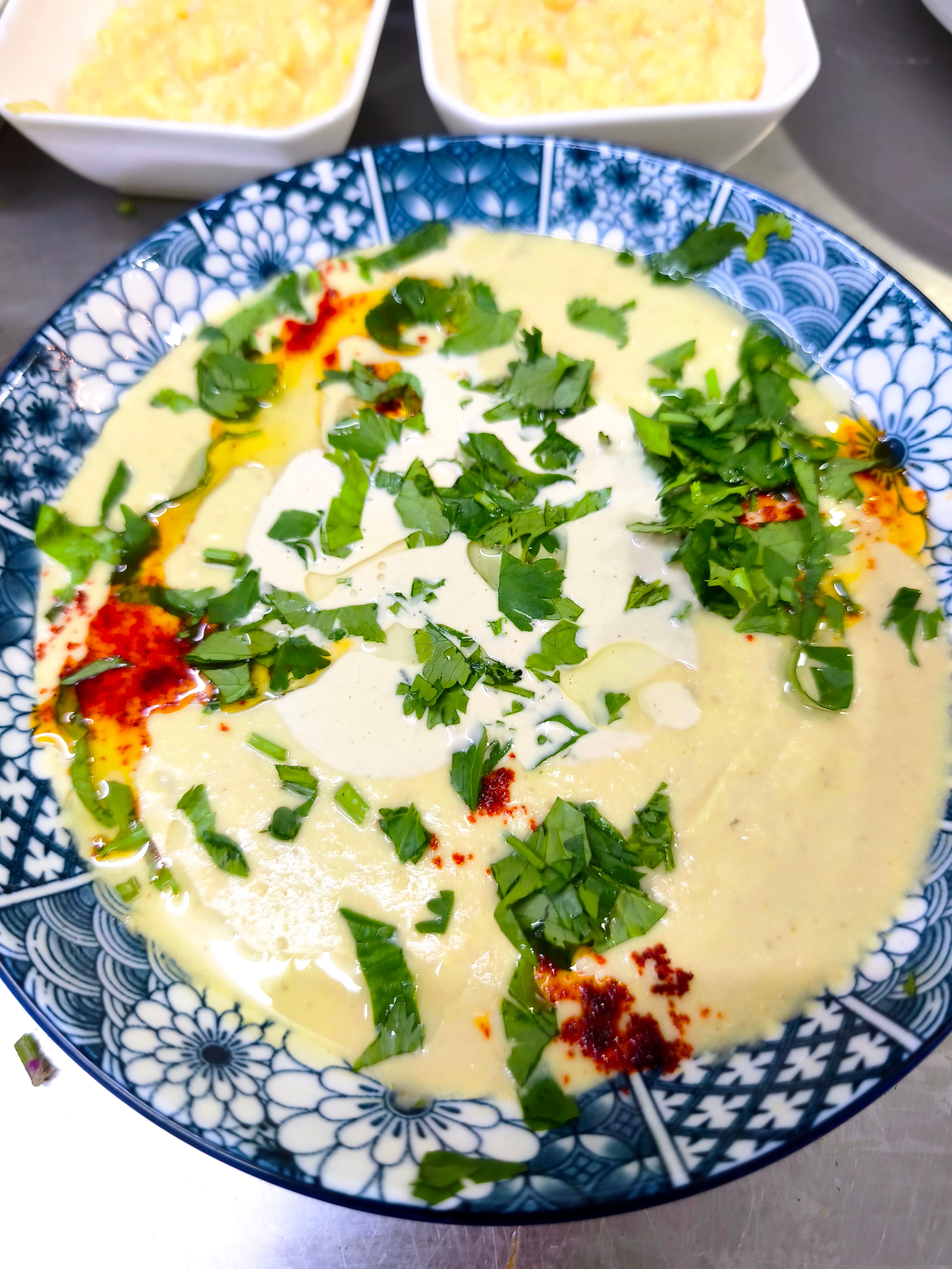 Creamy hummus with fresh cilantro, red paprika, and olive oil in a blue patterned bowl.