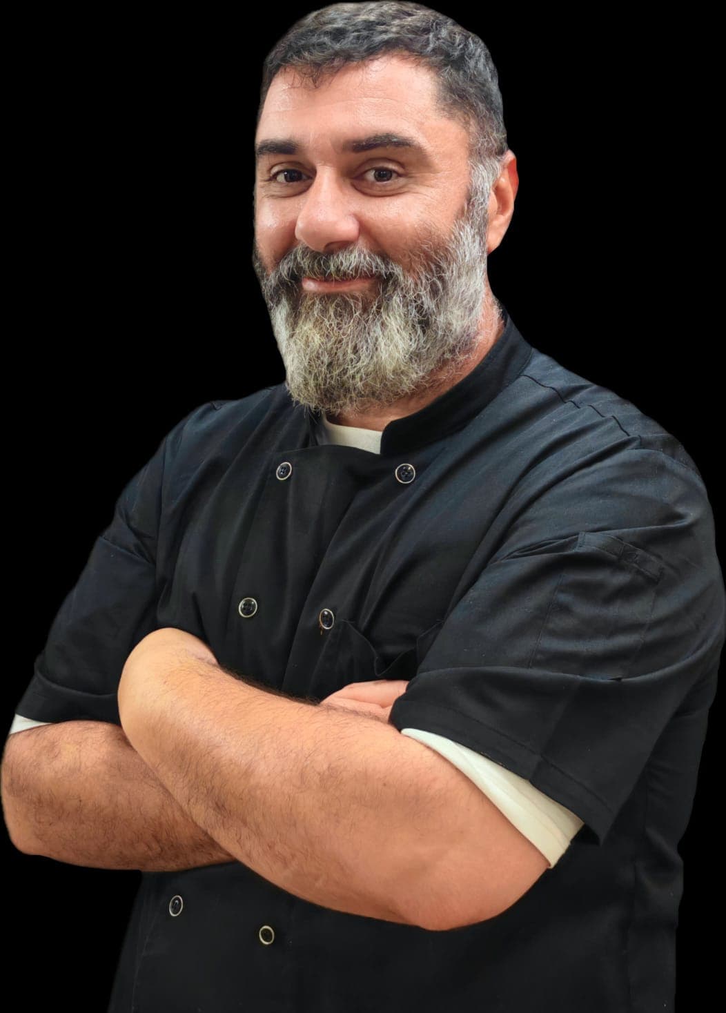Chef with a salt-and-pepper beard smiles, wearing a black jacket, arms crossed.