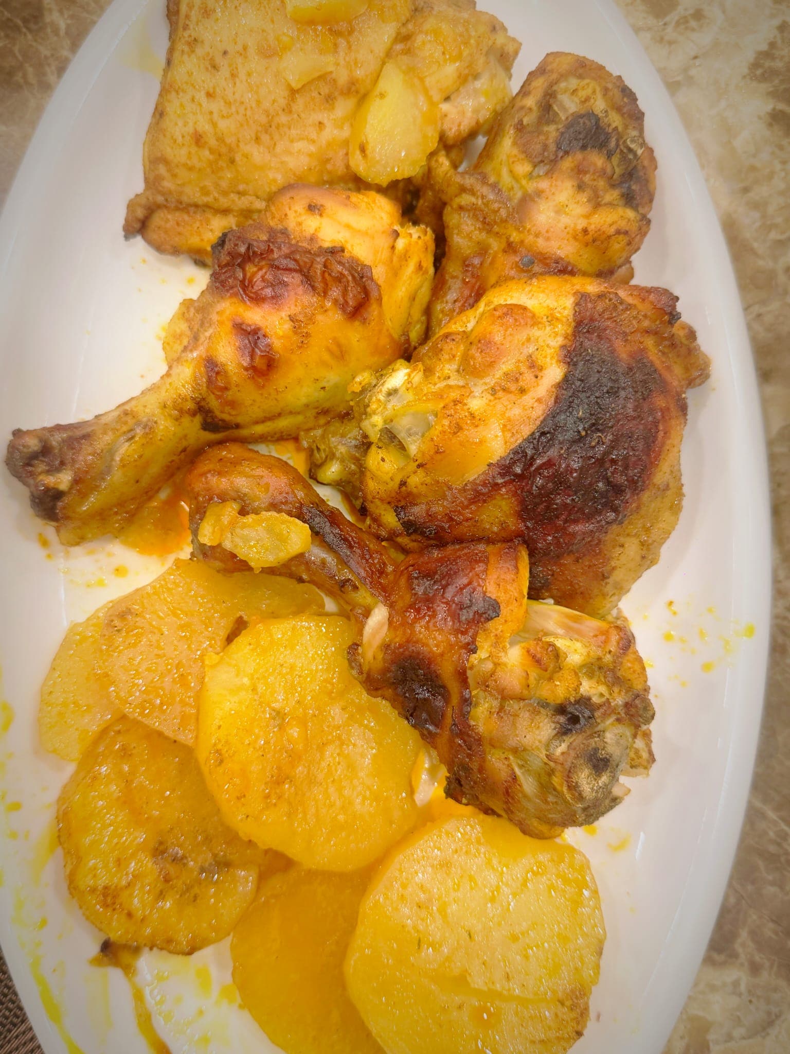 Roasted chicken drumsticks and thighs with golden, seasoned potato slices on a white plate.
