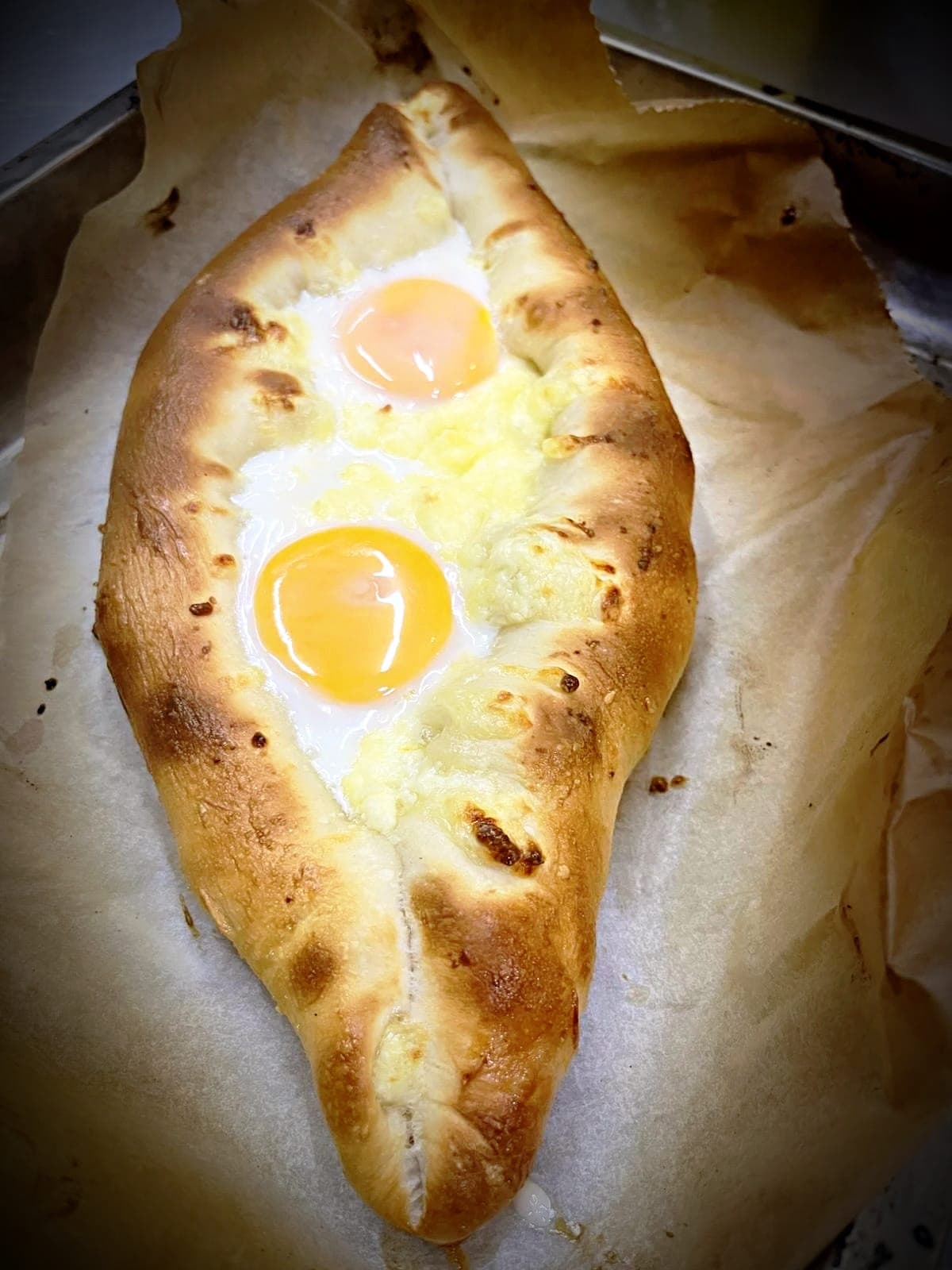 Georgian Adjaruli Khachapuri, a boat-shaped bread with gooey cheese and two bright egg yolks.
